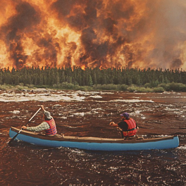 Cover image for Cory Smythe's Smoke Gets In Your Eyes - showing two people in a canoe paddling past a forest fire.